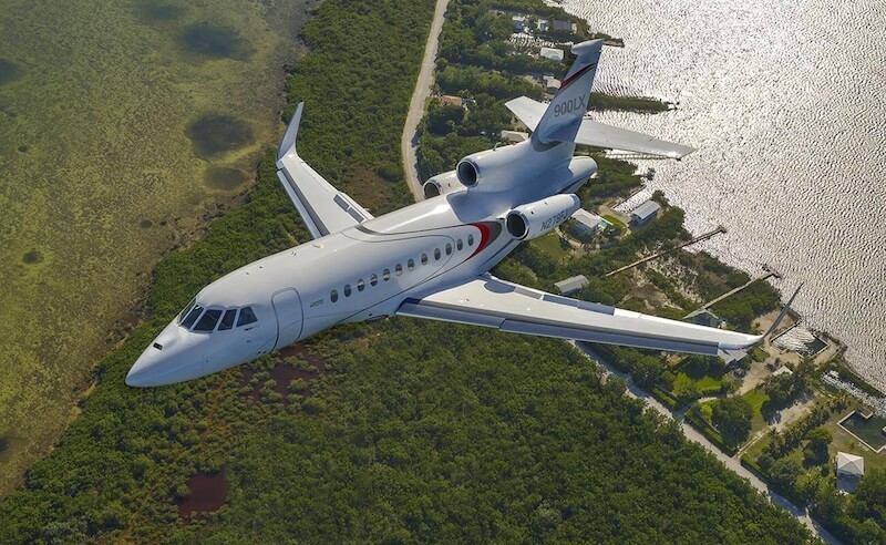 A private jet flying over a coastal landscape with greenery and a body of water.