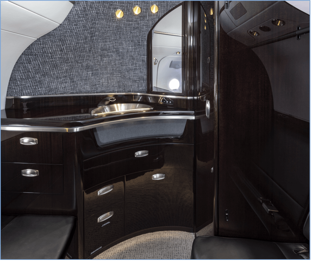 Cessna Citation Latitude lavatory with glossy dark wood cabinet paneling, silver fixtures and a small mirror. 