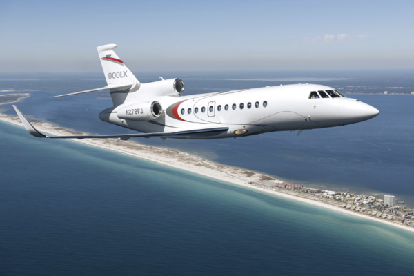 Dassault Falcon 900LX with red and gray striped exterior design flying over an isthmus in the middle of a vast blue ocean. 