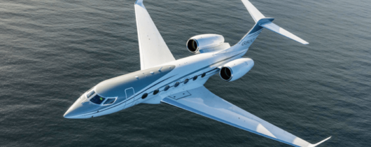 Gulfstream G500 with a standard silver paint scheme flying over a body of water.