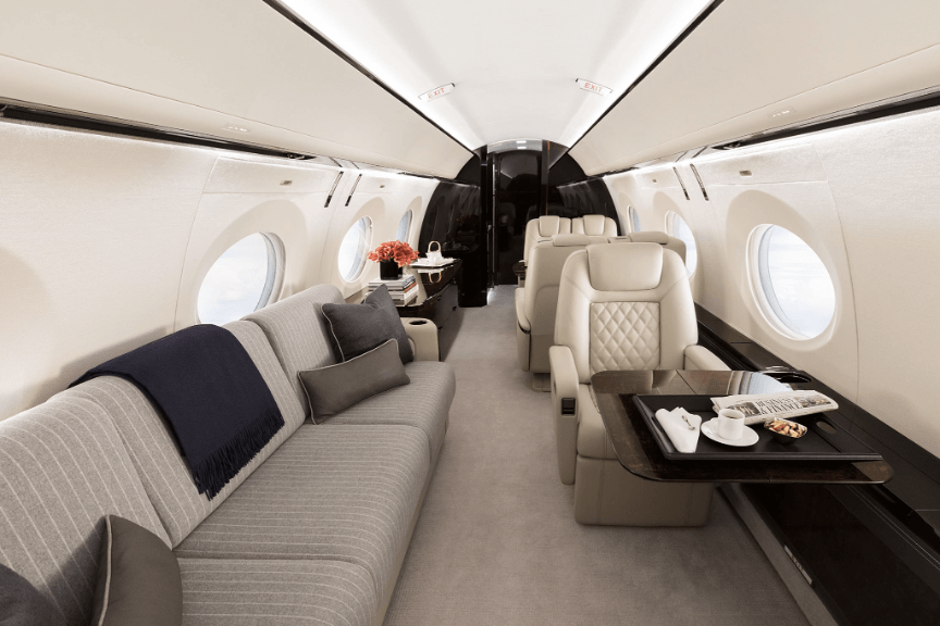 The Gulfstream G500’s aft cabin. To the left sits a berthable divan. with gray striped fabric. To the right is an execute-style seat upholstered in beige leather in front of a glossy dark wood table.