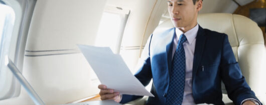 Man in a suit sitting on a flight with a laptop looking through papers