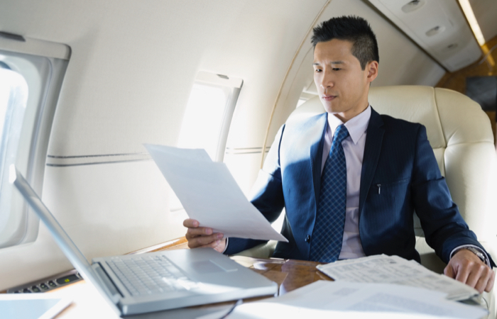 Man in a suit sitting on a flight with a laptop looking through papers
