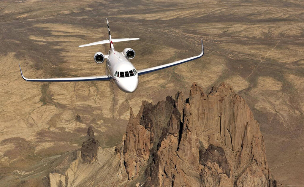 white private jet flys over brown desert landscape