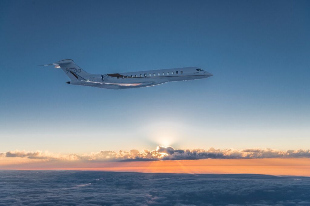 The image depicts a Global 7500 private jet flying high above the clouds during a beautiful sunset. The serene and expansive sky, marked by the soft hues of sunset and the expansive cloud cover, creates a breathtaking backdrop that emphasizes luxury and exclusivity. This visual is perfectly suited for an article discussing the best private jet events and conventions, as it encapsulates the prestige and high-end experience associated with private aviation. The jet itself, sleek and modern, serves as a symbol of the sophisticated and exclusive nature of these events, appealing to an elite audience interested in such luxurious gatherings.