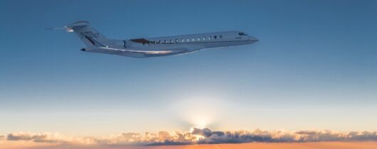 The image depicts a Global 7500 private jet flying high above the clouds during a beautiful sunset. The serene and expansive sky, marked by the soft hues of sunset and the expansive cloud cover, creates a breathtaking backdrop that emphasizes luxury and exclusivity. This visual is perfectly suited for an article discussing the best private jet events and conventions, as it encapsulates the prestige and high-end experience associated with private aviation. The jet itself, sleek and modern, serves as a symbol of the sophisticated and exclusive nature of these events, appealing to an elite audience interested in such luxurious gatherings.