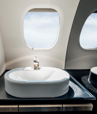 A raised, white porcelain sink sits on a black countertop below a sunny oval window. 