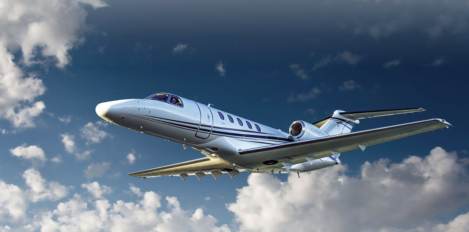 The-Cessna-Citation-CJ4-Gen2-with-dark-blue-stripe-detailing-flying-in-a-blue-sky-filled-with-soft-white-clouds. 