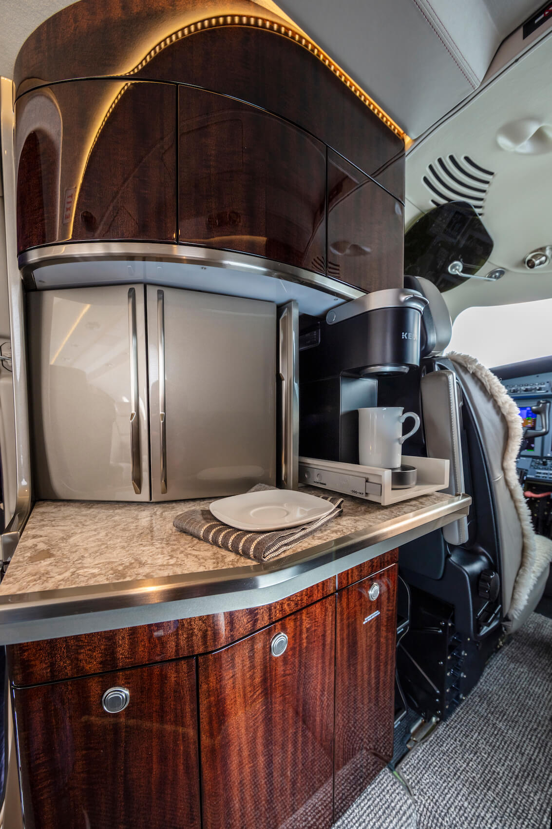 The-Cessna-Citation-CJ4-Gen2’s-galley-/-refreshment-center,-which-features-glossy,-dark-wood-paneling-and-a-coffee-machine.