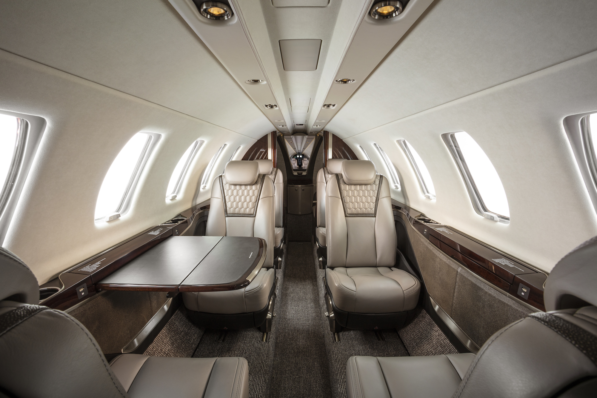 Main-cabin-of-the-Cessna-Citation-CJ4-Gen2,-with-four-executive-style-seats-upholstered-in-beige-leather-in-a-club-configuration.-A-retractable-table-is-partially-extended-on-one-side. 