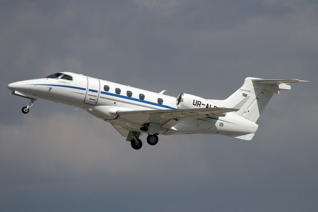 image of a white embraer 505 phenom 300 aerojet flying through a cloudy grey sky background